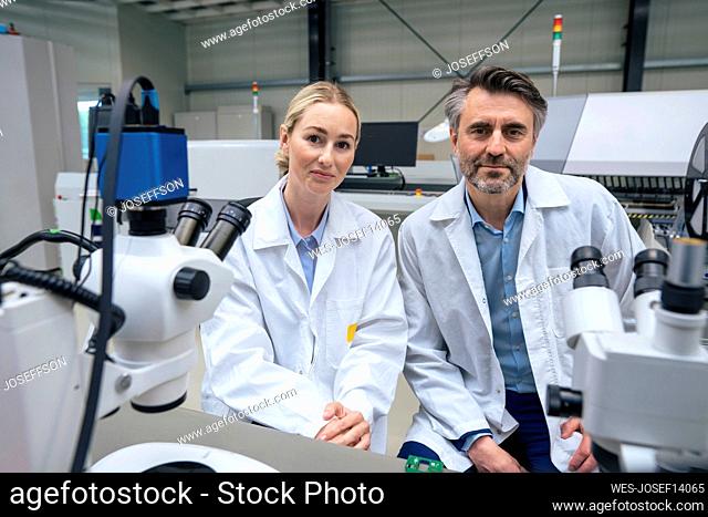 Smiling scientists wearing lab coat sitting in industry