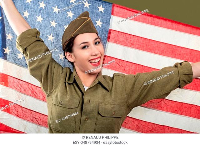 smiling young woman in US military uniform holding up an American flag