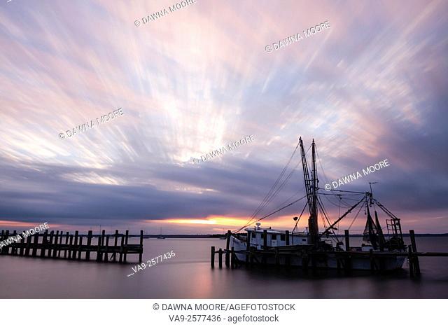 Long exposure sunset with clouds streaking by over a shrimp boat tied up to an old dock in Fernandina Beach, Florida