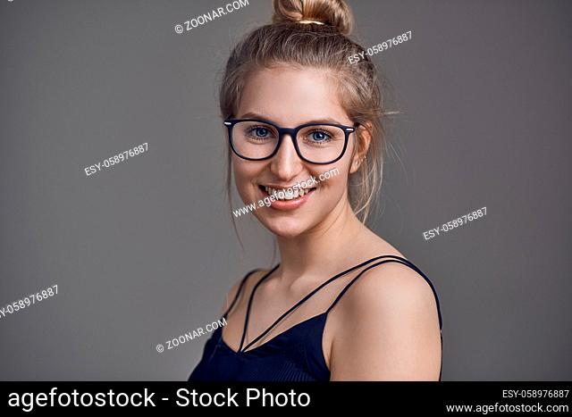 Attractive stylish blond woman with her hair in a bun wearing glasses smiling at the camera