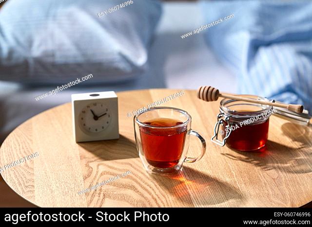 cup of tea, honey and alarm clock on table