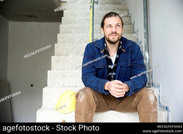 Thoughtful construction worker sitting on steps in house under construction