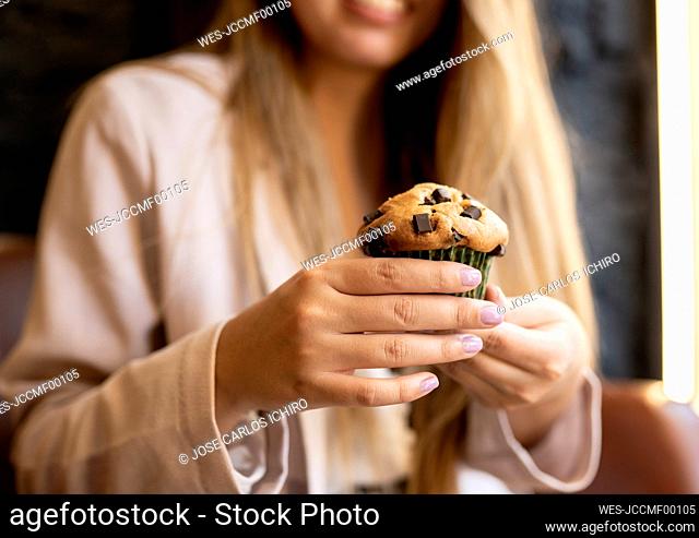 Woman holding chocolate chip muffin while sitting at cafe