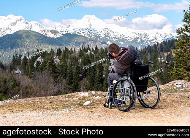 photo of a man on wheelchair using camera in nature, photographing beautiful mountains