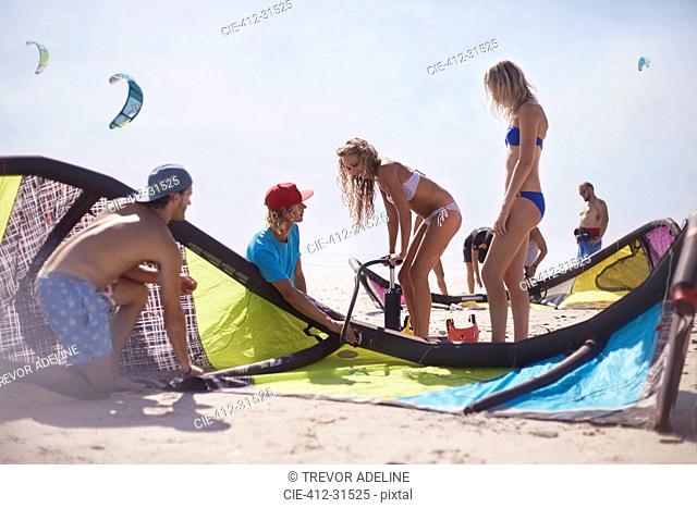 Friends preparing kiteboarding kite on sunny beach