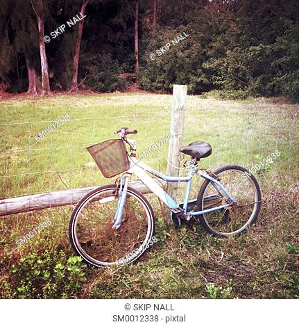 A bicycle sitting beside a barb wire fence in the countryside