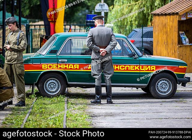 24 July 2020, Saxony-Anhalt, Beuster: A visitor in the uniform of the GDR People's Police stands in front of a Lada of the Soviet Military Police during the...
