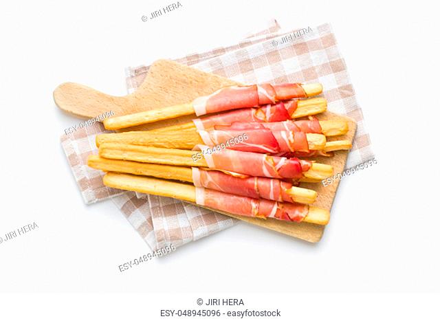 Parma ham prosciutto with grissini breadsticks on cutting board isolated on white background