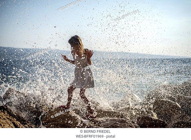 Croatia, Lokva Rogoznica, girl walking through splashing sea foam on rocks