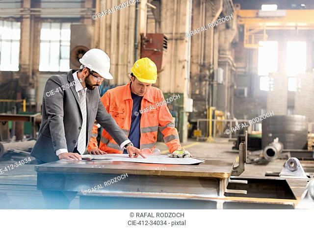 Manager and steel worker engineer reviewing blueprints in factory