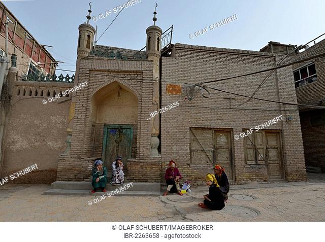 Muslim women, Uighurs with colourful headscarves sitting in front of a mosque, mud-brick houses, Uighur historic centre of Kashgar, Silk Road, Xinjiang, China
