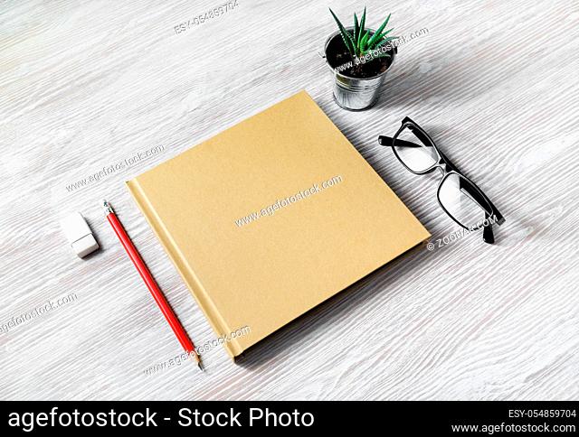 Blank stationery template. Closed blank sketchbook, glasses, pencil, eraser and plant on light wood table background