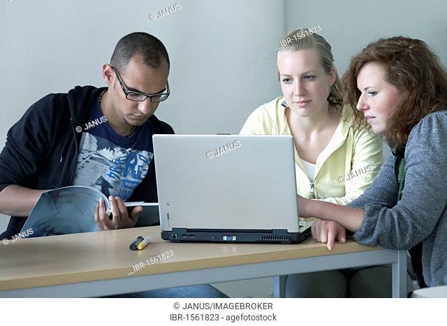Three young adults talking while on a laptop, work