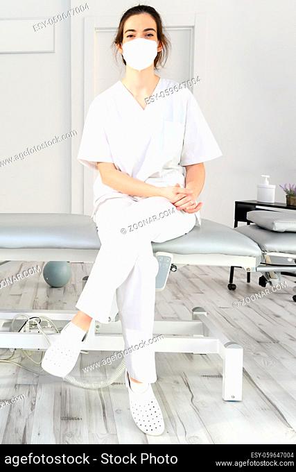 Friendly female physiotherapist posing in modern clinic wearing protective face mask during coronavirus pandemic. High quality photo