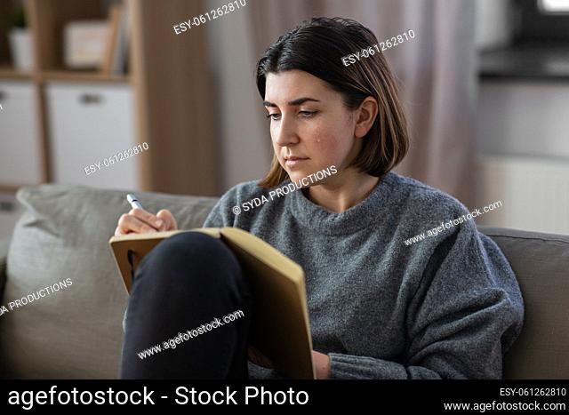 crying woman with diary sitting on sofa at home