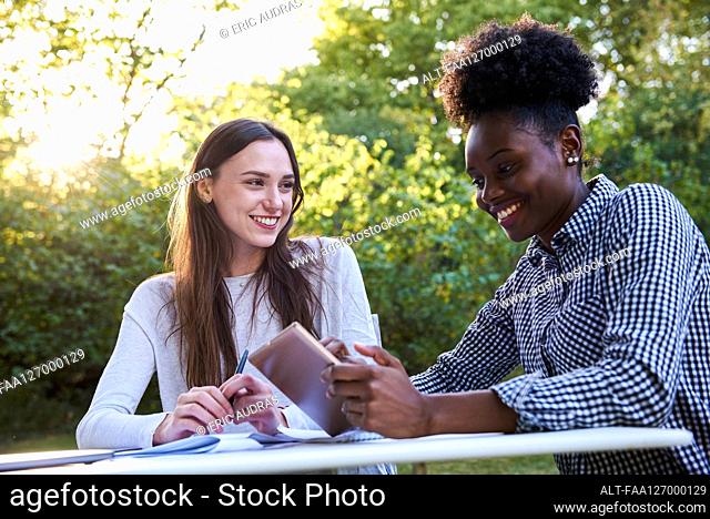 Smiling young friends using digital tablet while studying in park, Orgeval