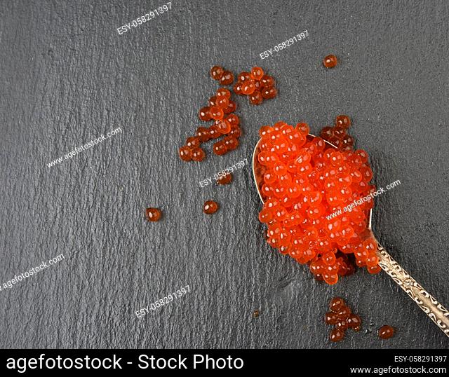 red caviar of chum salmon in a metal spoon on a black background, top view, close up