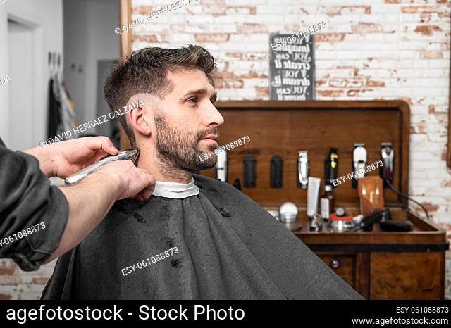 Man barber cutting hair of male client with clipper at barber shop. Hairstyling process. High quality photography