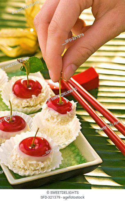 Hand holding a chocolate-dipped cherry with grated coconut