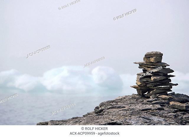Rock inukshuk on a ledge backdropped by pack ice veiled by fog in the Strait of Belle Isle, Labrador Coastal Drive, Viking Trail, Southern Labrador
