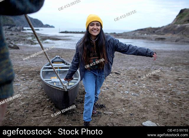 Portrait happy young woman pulling canoe on beach