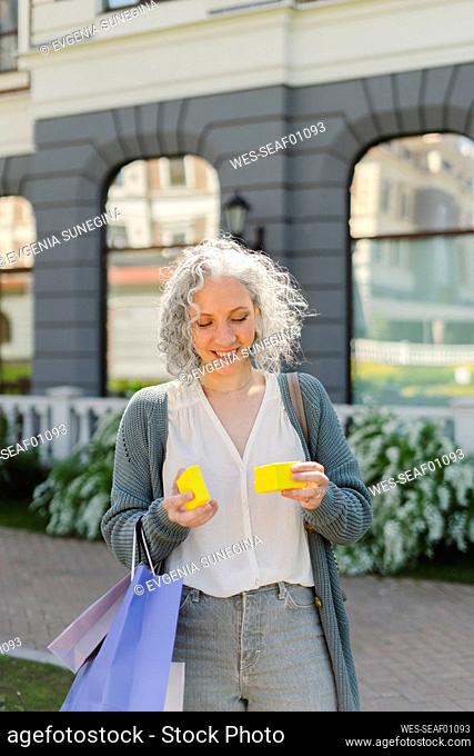 Smiling woman looking at yellow gift box in front of building