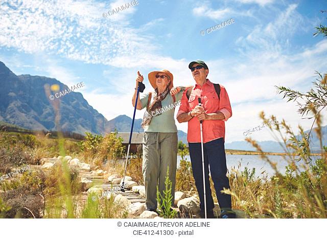 Active senior couple hiking with hiking poles at sunny summer lakeside