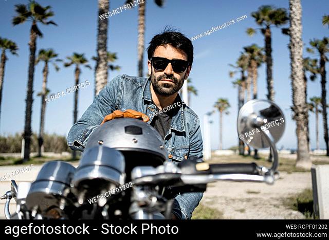 Handsome young man with helmet sitting on motorcycle during sunny day