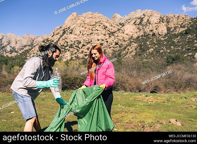 Man and woman with garbage bag collecting plastic bottle on sunny day
