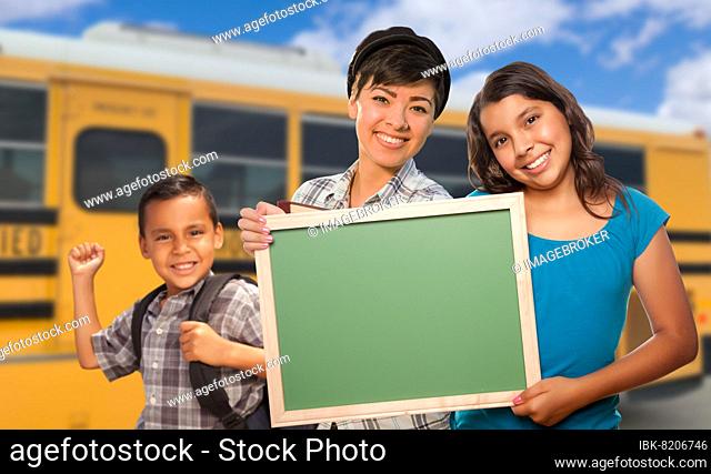 Young mixed-race students with blank chalkboard near school bus