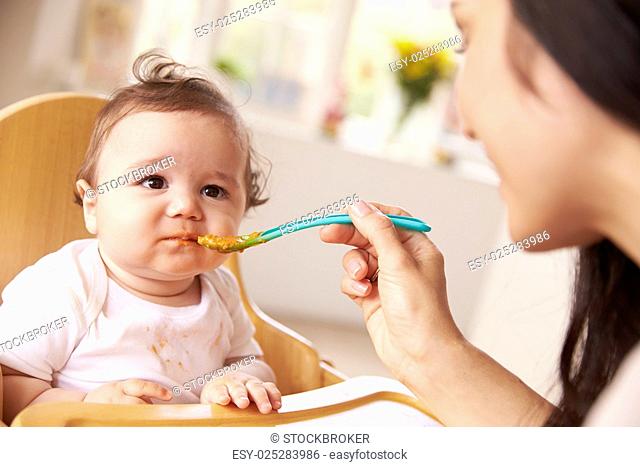 Happy Baby Being Fed In High Chair At Meal Time