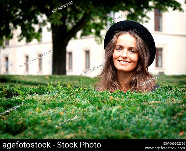 happy smiling young woman in a park looking over hedge