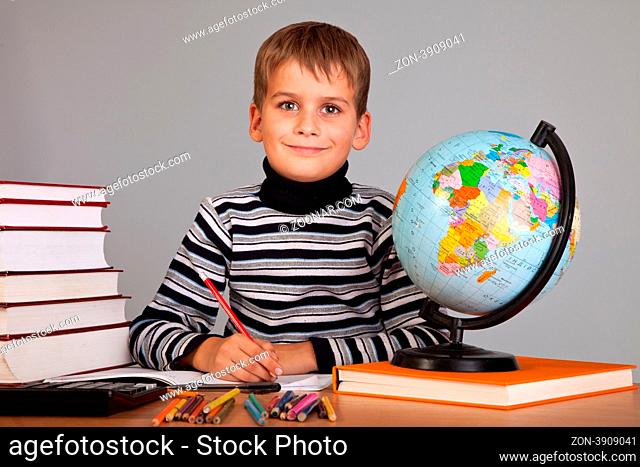Cute schoolboy is writting isolated on a gray background
