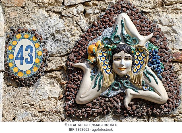 The symbol of Sicily, a girl's head surrounded by snakes and small wings with three running angled legs, sun wheel, on a wall, Taormina, Messina, Sicily, Italy
