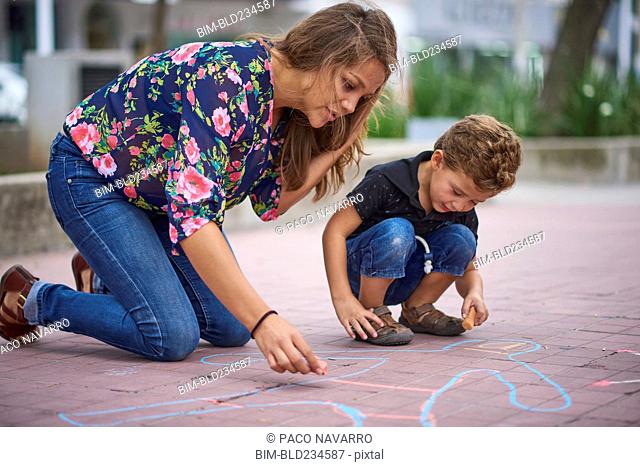 Hispanic mother and son drawing on sidewalk with chalk