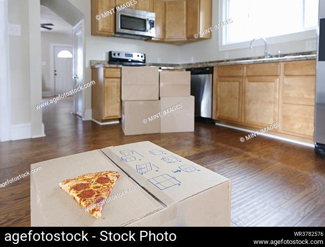 Moving house, relocation, cardboard boxes piled up in a house fitted kitchen, a slice of pizza
