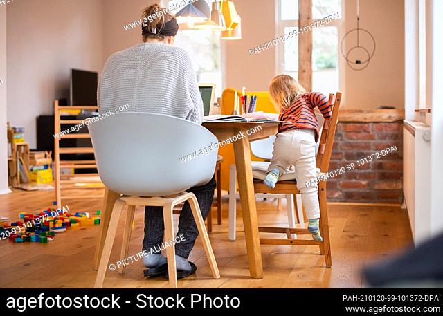 20 January 2021, Lower Saxony, Hanover: A two-year-old child climbs onto a chair next to his mother, who is working on a laptop in her home office