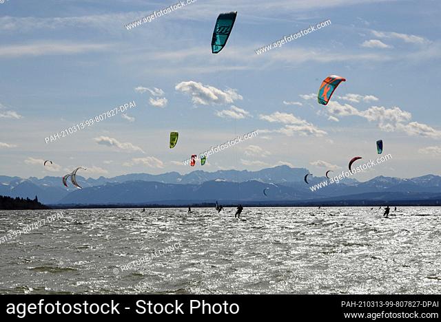 13 March 2021, Bavaria, Hersching: Kitesurfers glide over the Ammersee during a storm low in front of the snowy alpine scenery
