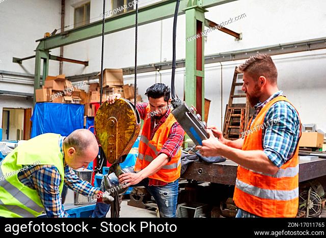 Arbeiter Team in der Fabrikhalle befestigt Last an Kranhaken in der Fabrik für Metallbau