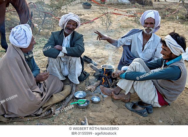 Four Indian men in turbans sitting on the ground having a conversation, milk tea is being prepared over an open fire, Pushkar Camel Fair
