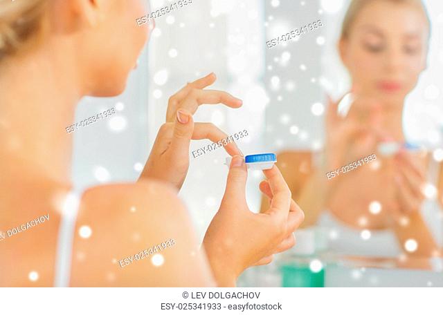 beauty, vision, eyesight, ophthalmology and people concept - close up of young woman applying contact lenses at mirror in home bathroom over snow