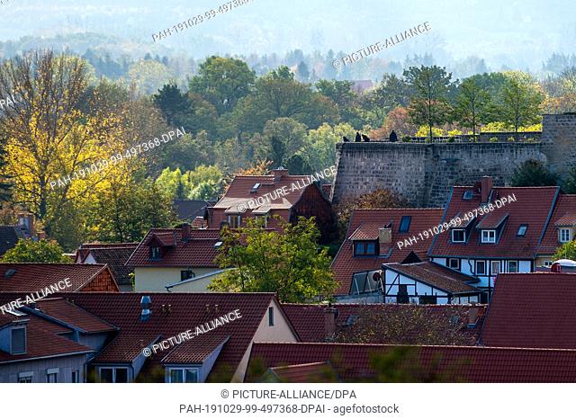 29 October 2019, Saxony-Anhalt, Quedlinburg: Trees with autumnal leaves surround the houses of the city. On the terrace of the Schlossberg there are visitors...