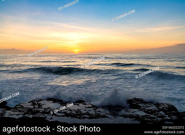 View of large waves crashing onto rocky shore with tidal pools at sunset