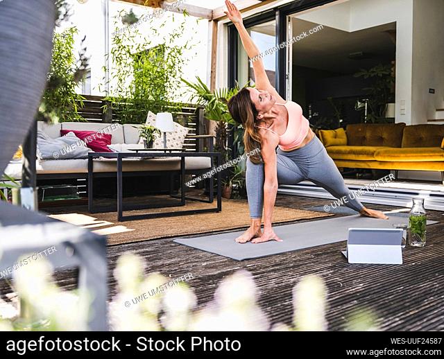 Woman practicing Trikonasana on exercise mat on terrace