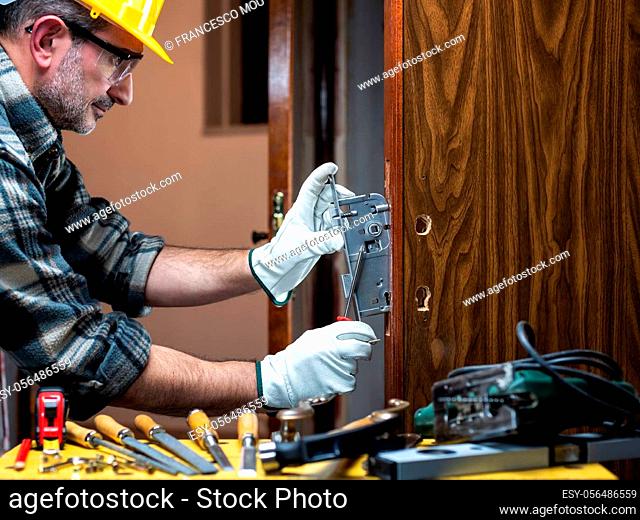 Close-up. Carpenter at work repairs and installs the new lock of a wooden door. Construction industry