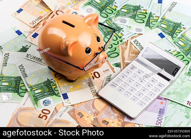Piggy Bank on Euro Banknotes With White Calculator. European Health Insurance Costs