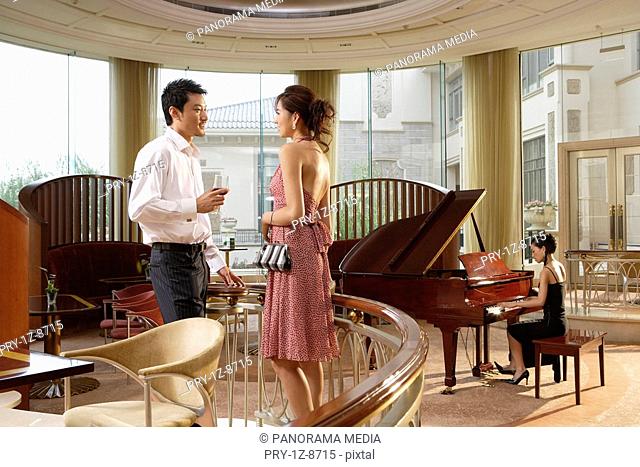 Couple standing near banister while young woman playing piano in restaurant