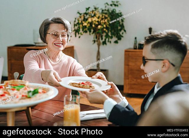 Happy grandmother giving slice of pizza to grandson at cafe