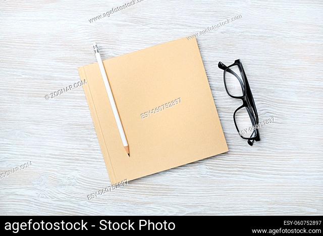 Photo of blank closed sketchbook, pencil and glasses on wooden background. Responsive design mockup. Top view. Flat lay