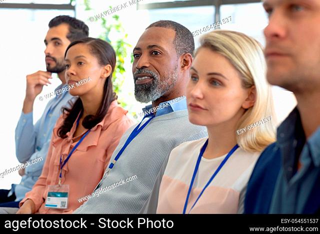 Side view of a diverse group of business creatives sitting in a row in the audience at a business conference listening
